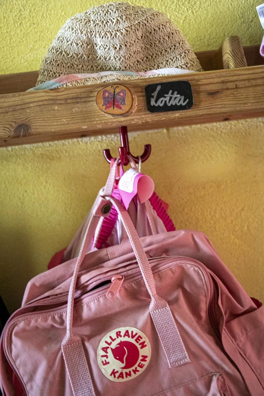 Kindergarderobe mit Strohhut und rosafarbenem Rucksack an gelber Wand