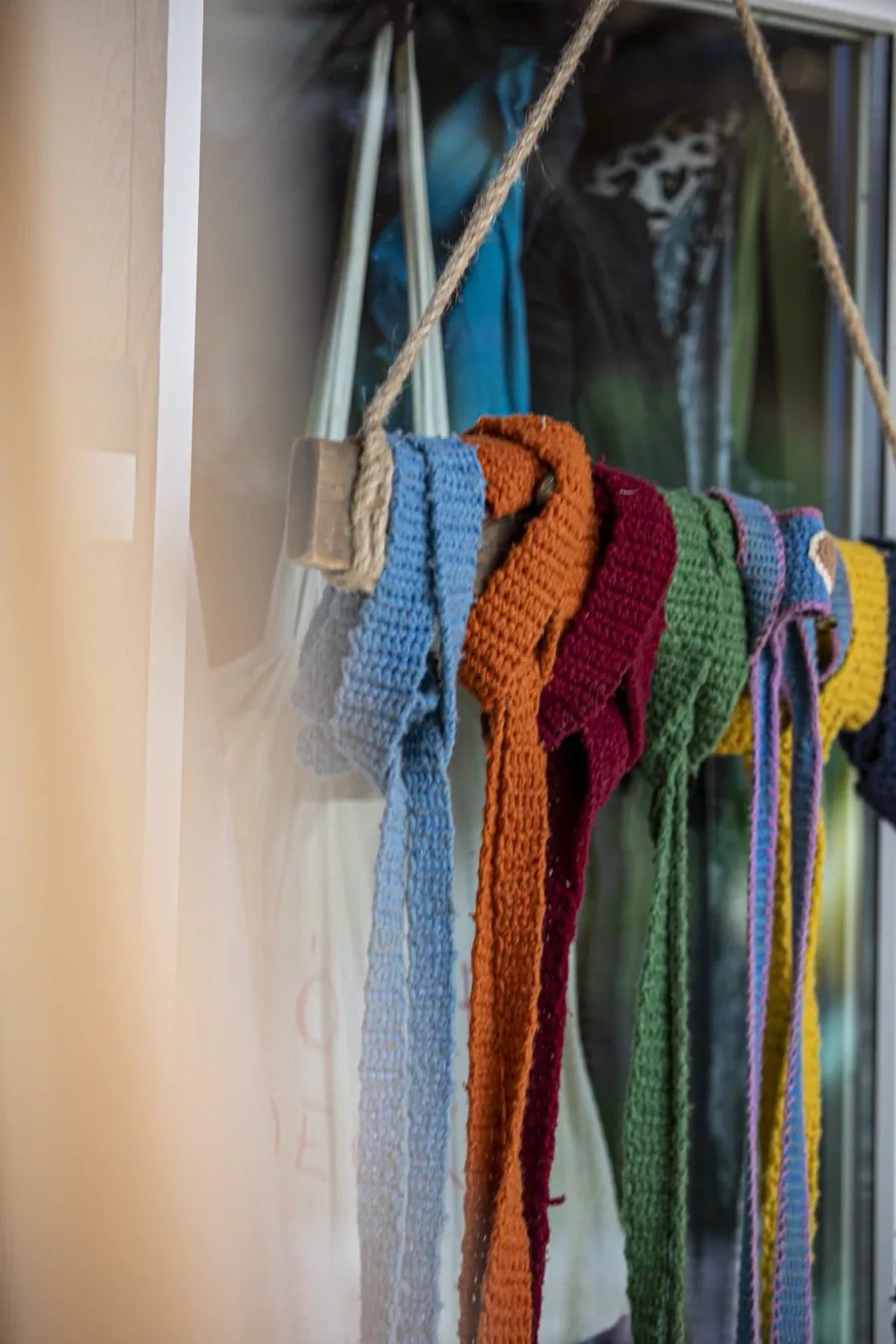 Bunte gehäkelte Bänder hängen an einer Holzstange vor dem Fenster