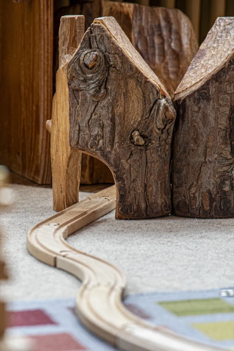 Geschnitzte Holzhäuschen mit Holzeisenbahn-Schienen auf dem Teppich