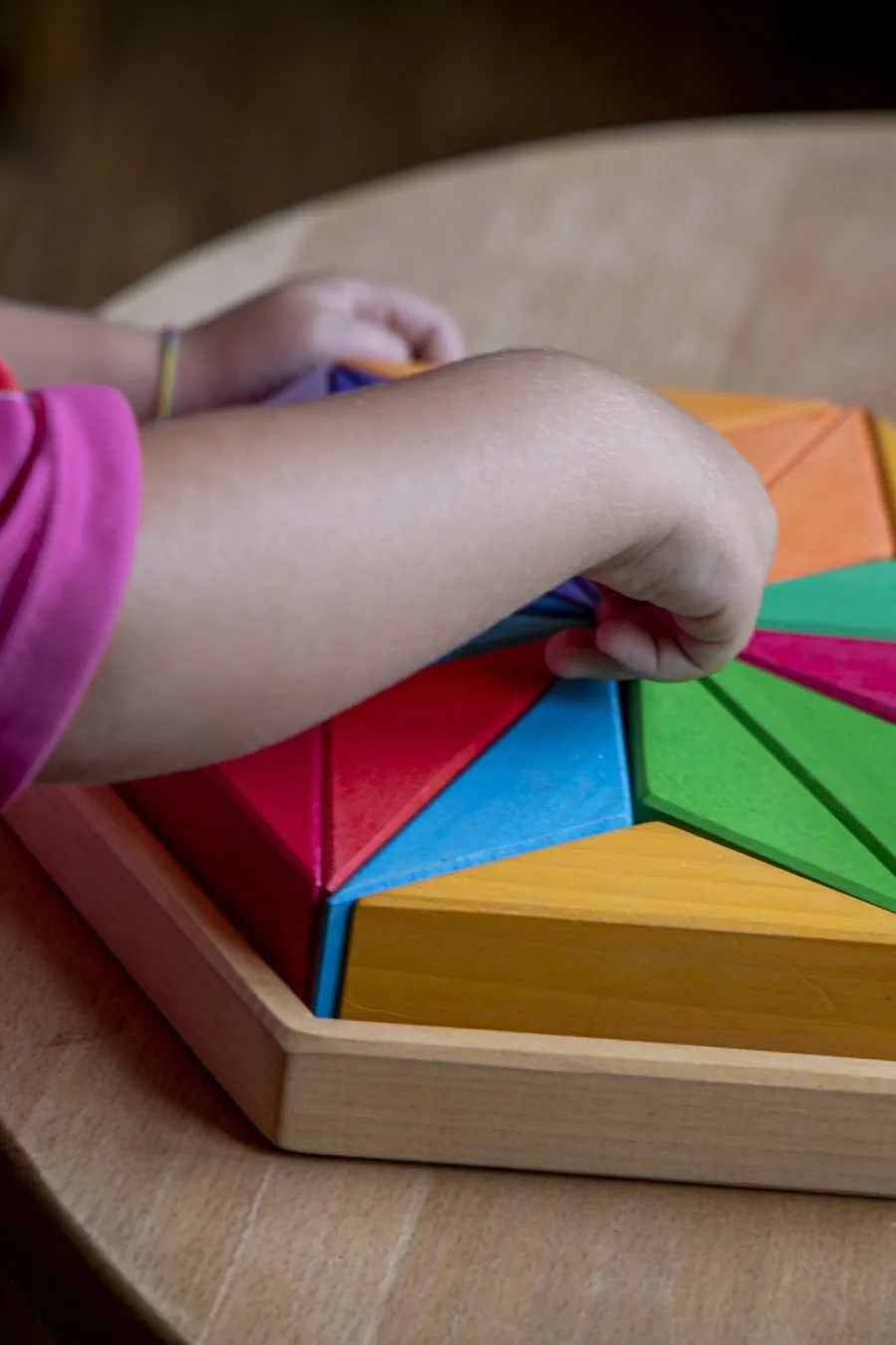 Kinderhand greift nach einem bunten Holz-Regenbogenpuzzle
