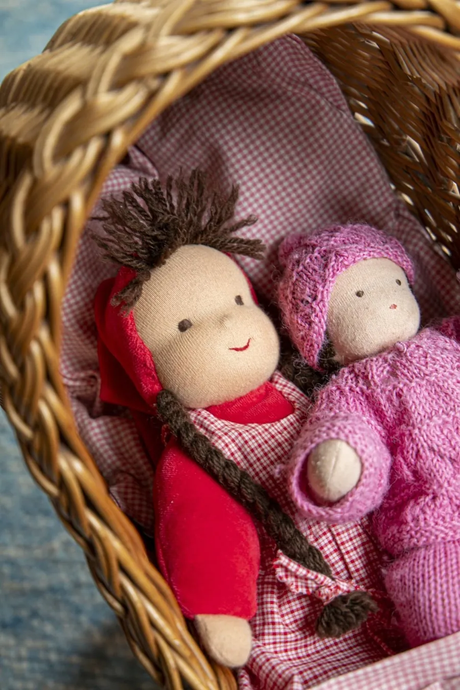 Zwei Waldorfpuppen in rotem und rosafarbenem Strickzeug in einem Weidenkorb