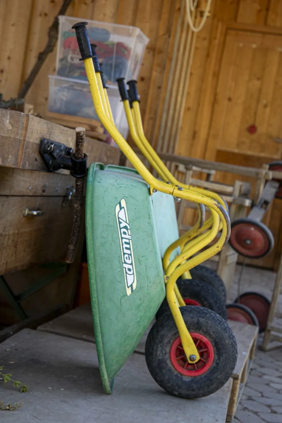 Grüne Kinder-Schubkarre mit gelben Griffen an der Werkbank im Gartenschuppen