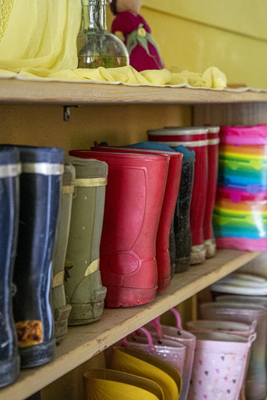 Bunte Gummistiefel der Kinder, aufgereiht im Garderobenregal