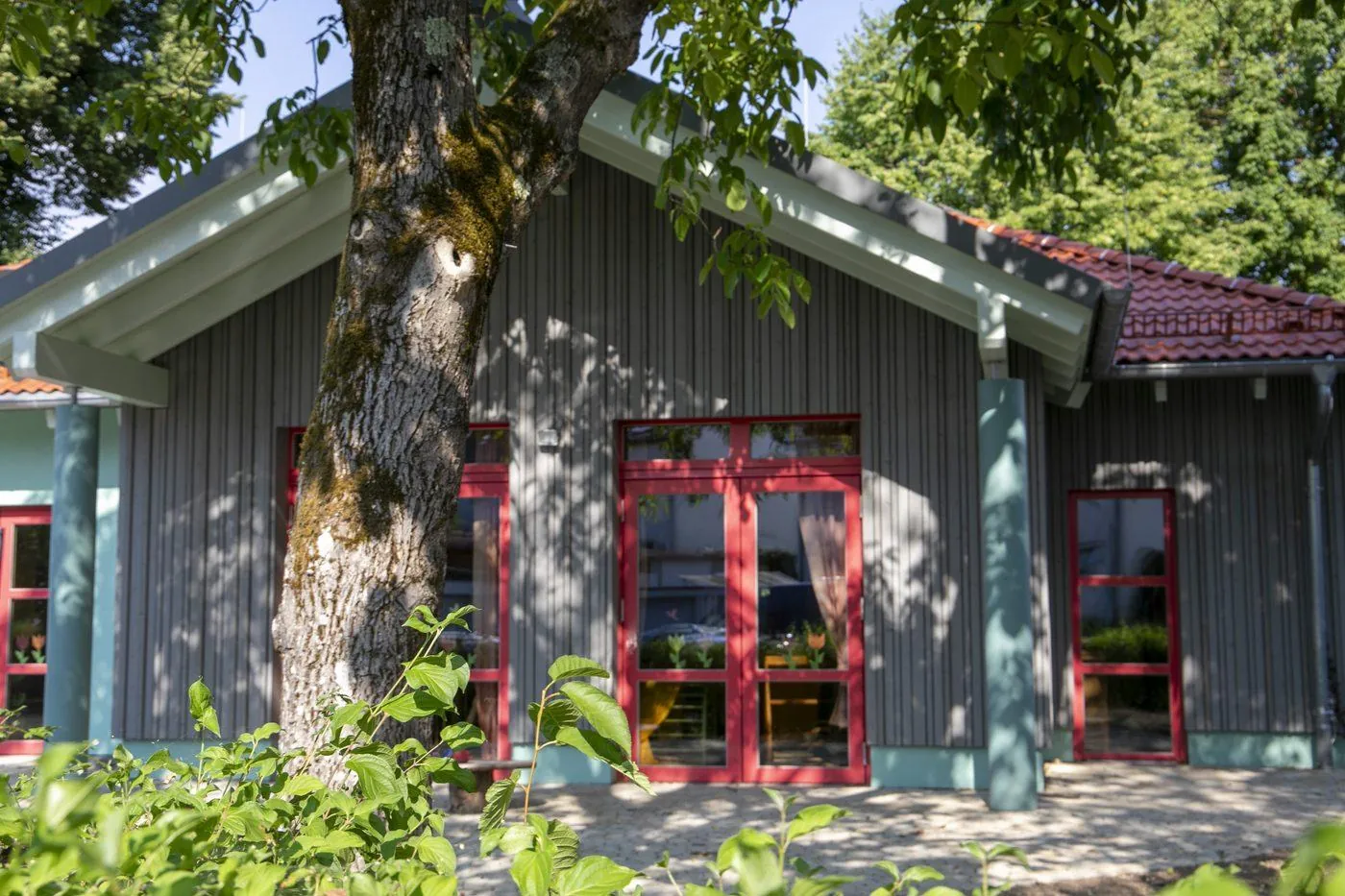 Der 2025 neu gebaute Gruppenraum in Großdeinbach mit roten Türen unter einem alten Baum