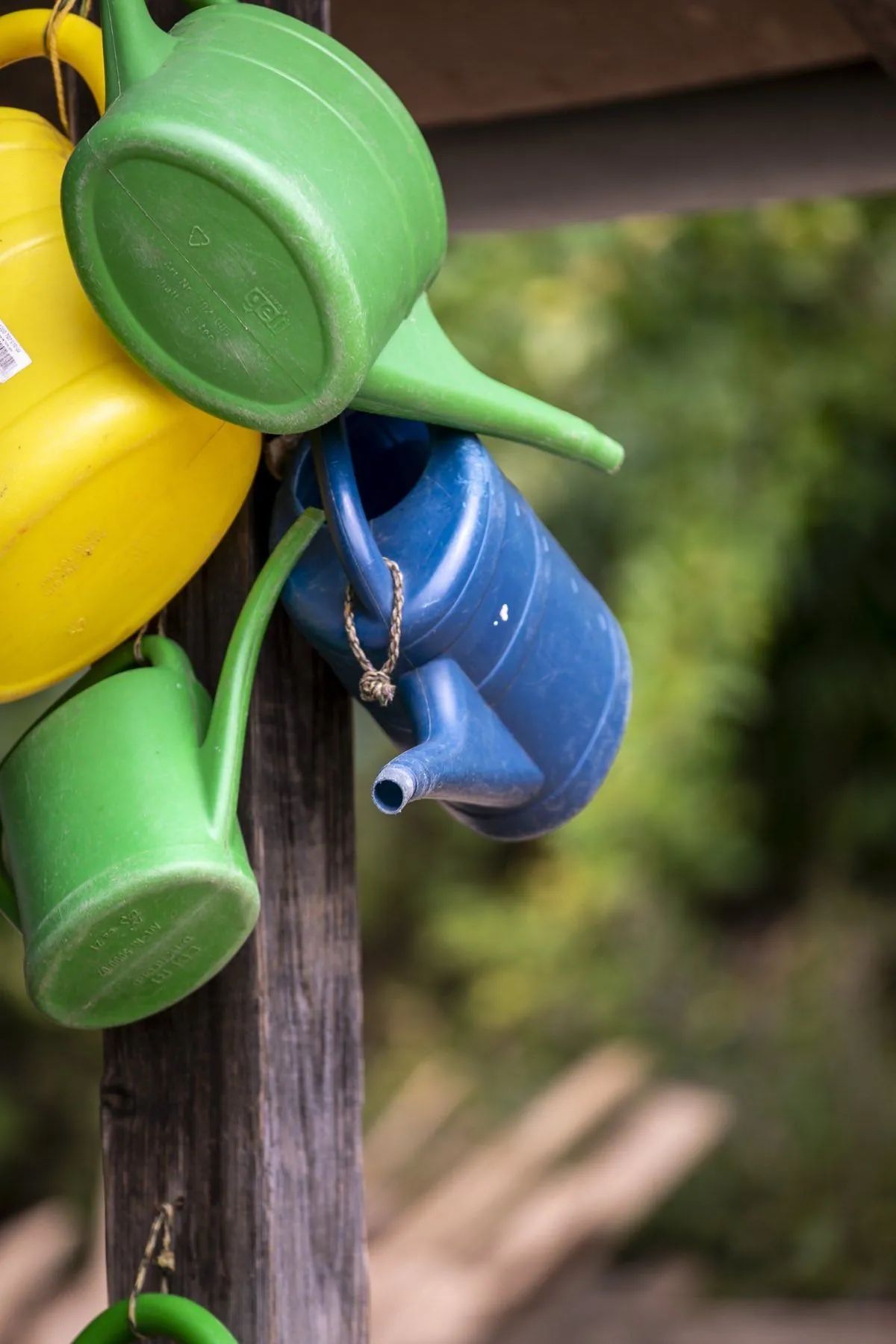 Bunte Gießkannen an einem Holzpfosten im Garten
