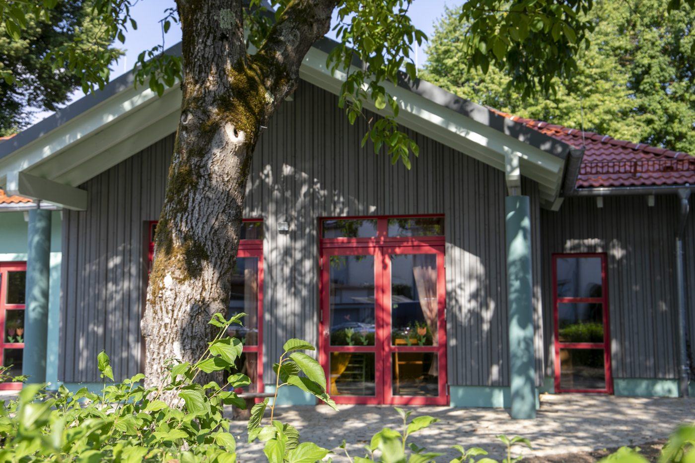 Der 2025 neu gebaute Gruppenraum in Großdeinbach mit roten Türen unter einem alten Baum